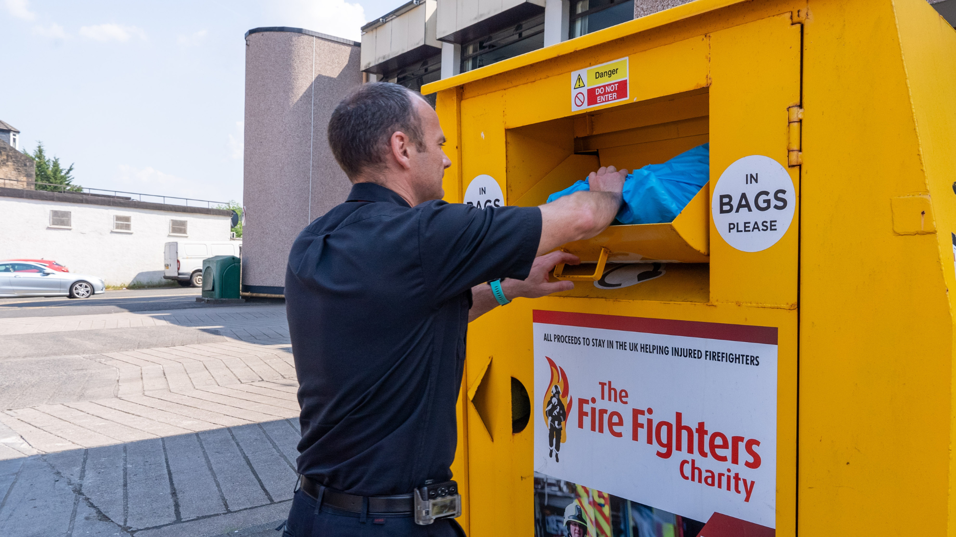 A man places a blue bag into a yellow donation bin labelled 