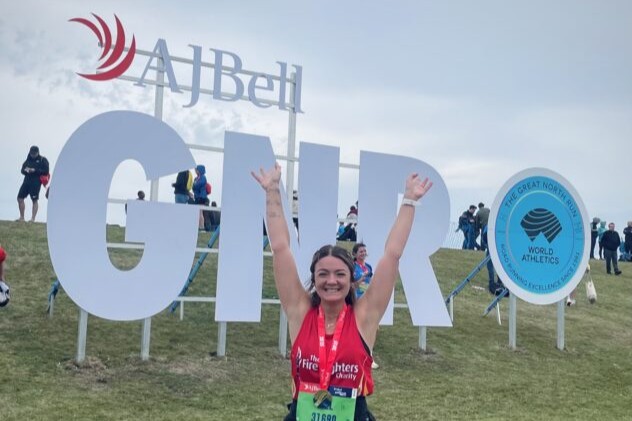 A smiling runner with arms raised stands in front of large 