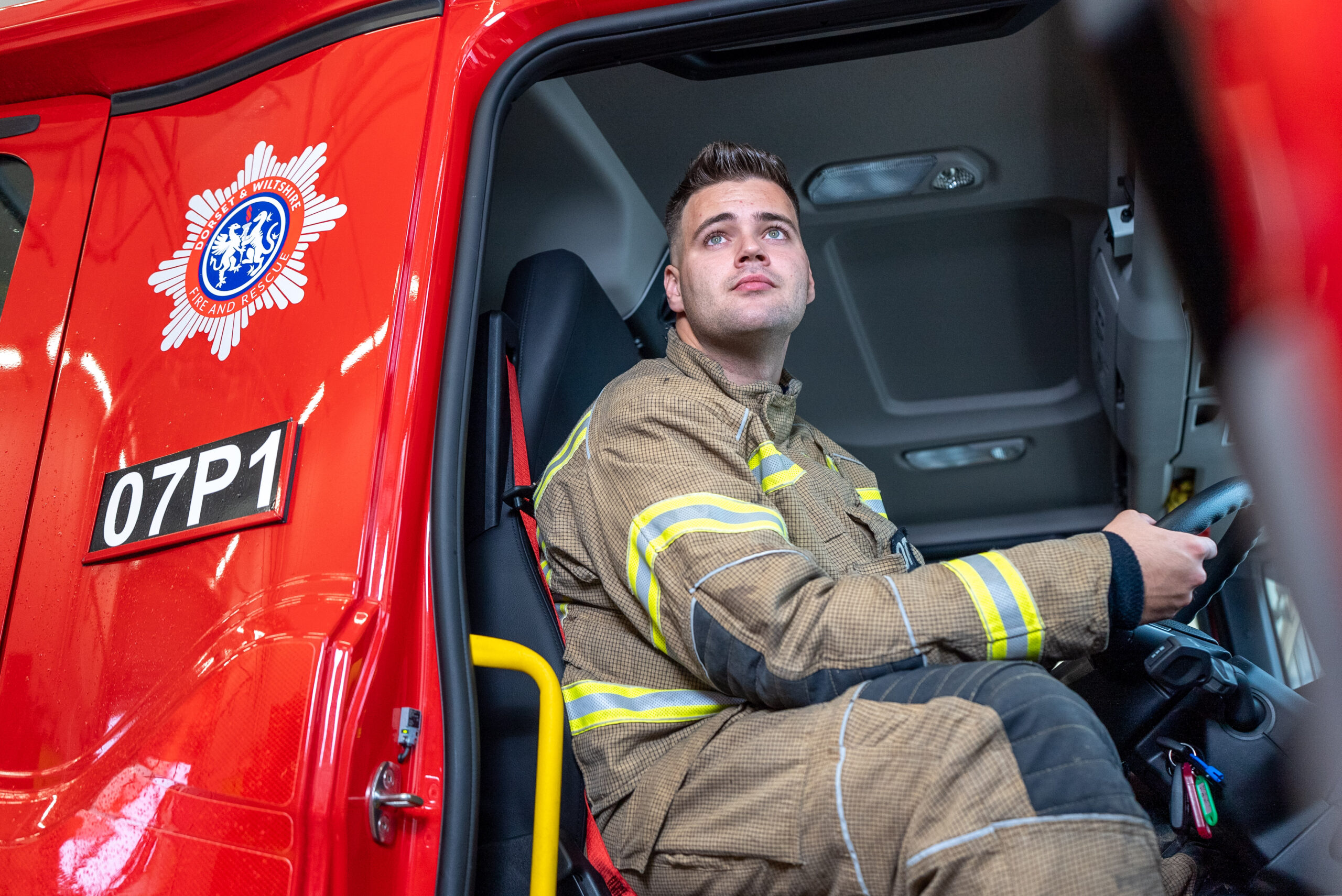 Firefighter for Dorset sitting in the driving seat of a fire engine in the bay with the door open looking up in contemplation.