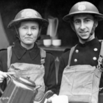 Two firefighters in uniform and helmets stand beside a vehicle. One holds a metal kettle and the other a mug, both smiling. The background includes a jug and cups. Text reads: Copyright London Fire Brigade.