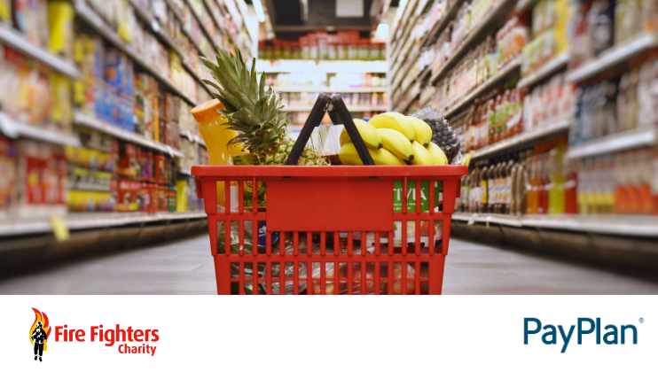 A red grocery basket filled with various fruits and food items sits on a supermarket aisle floor. The Fire Fighters Charity and PayPlan logos are at the bottom of the image.