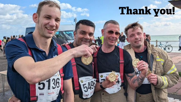 Four men in firefighter uniforms and race bibs smile and hold up medals by the seaside. The words 