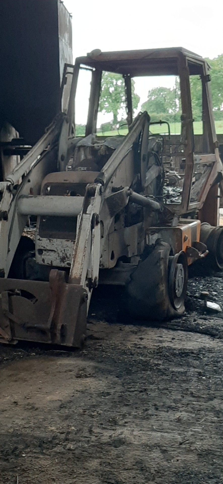 A fire-damaged skid steer loader parked in a shed.